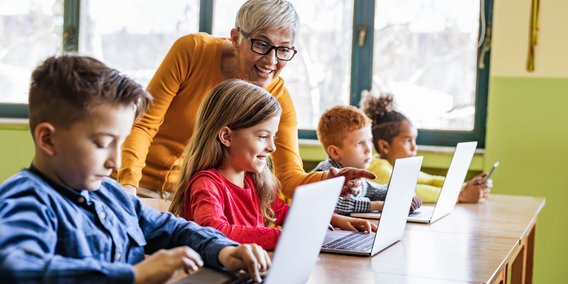 Lehrerin hilft Schüler/innen am Computern im Klassenraum